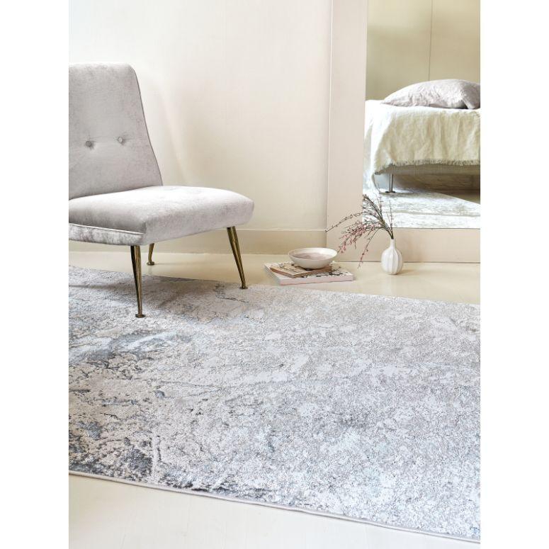 Grey patterned rug on light floor beside velvet accent chair in modern living space