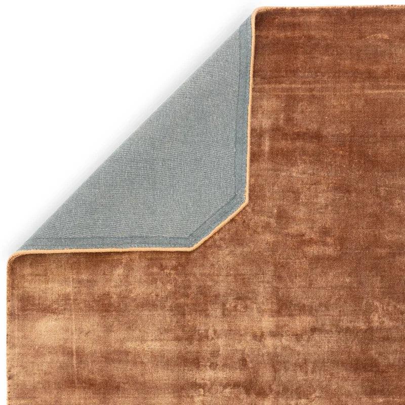 Brown velvet area rug with grey fabric backing shown in corner fold detail