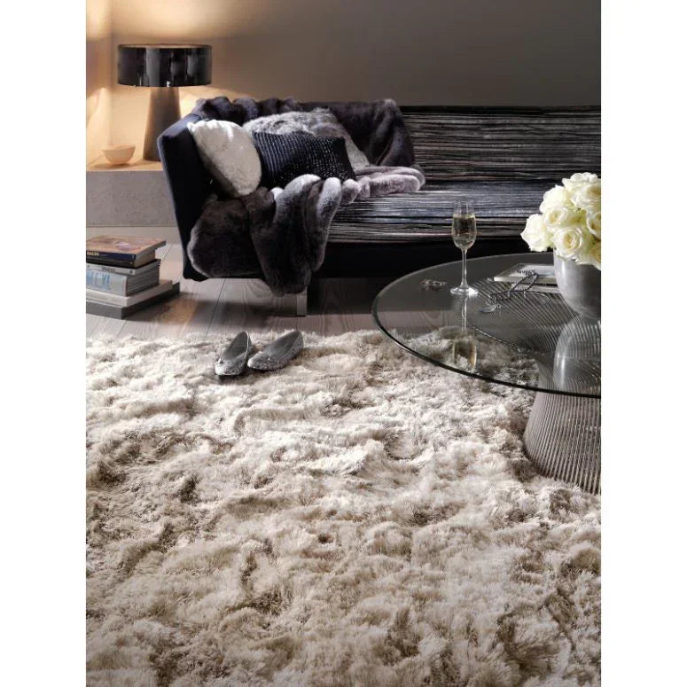 Cream shaggy rug in living room with glass coffee table, sofa, and decorative cushions