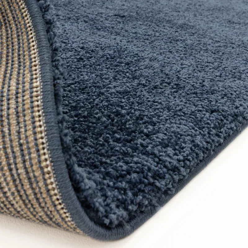 Close-up of navy blue textured rug with soft pile and woven backing on white floor