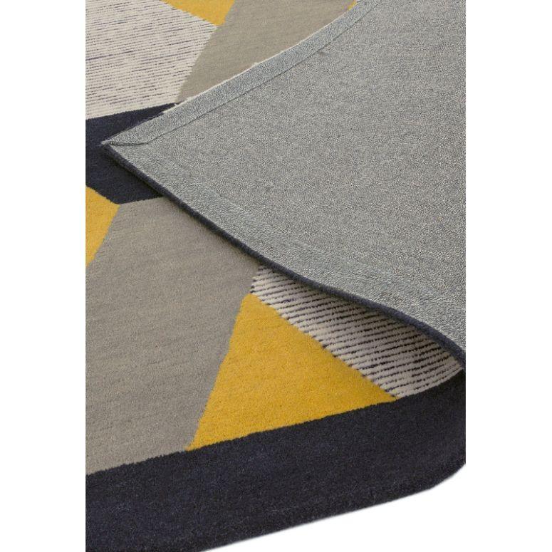 Geometric area rug with grey, yellow, navy shapes and corner lifted showing backing detail
