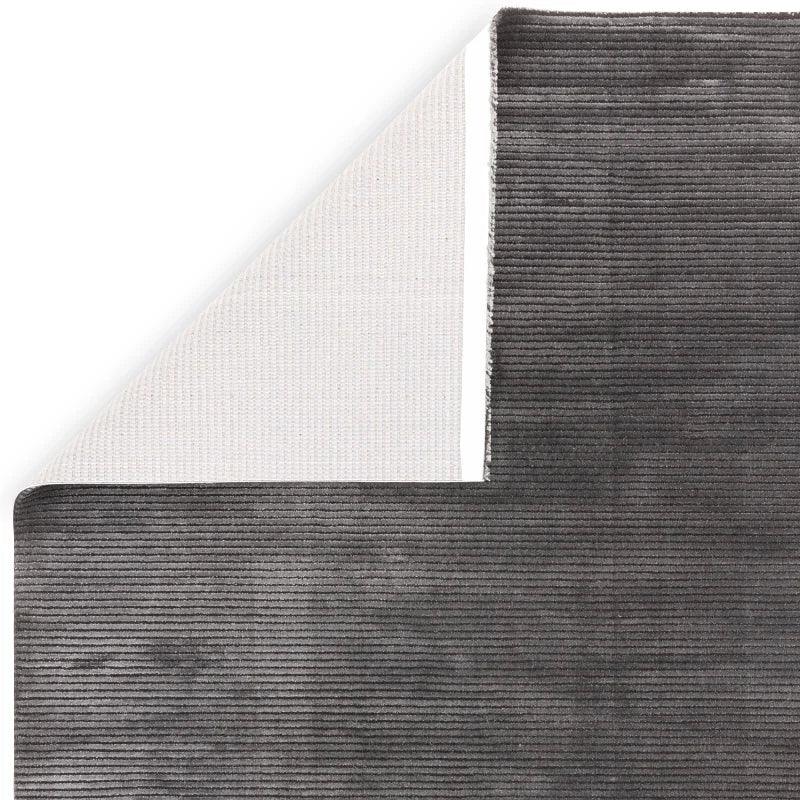 Charcoal grey ribbed area rug with corner folded to show backing