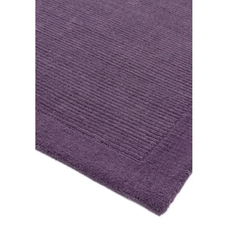 Purple ribbed bath mat with textured border, close corner detail on white background