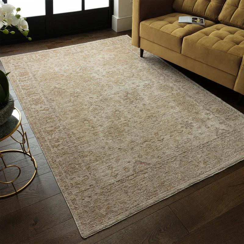Beige patterned area rug on dark wood floor beside mustard sofa in living room
