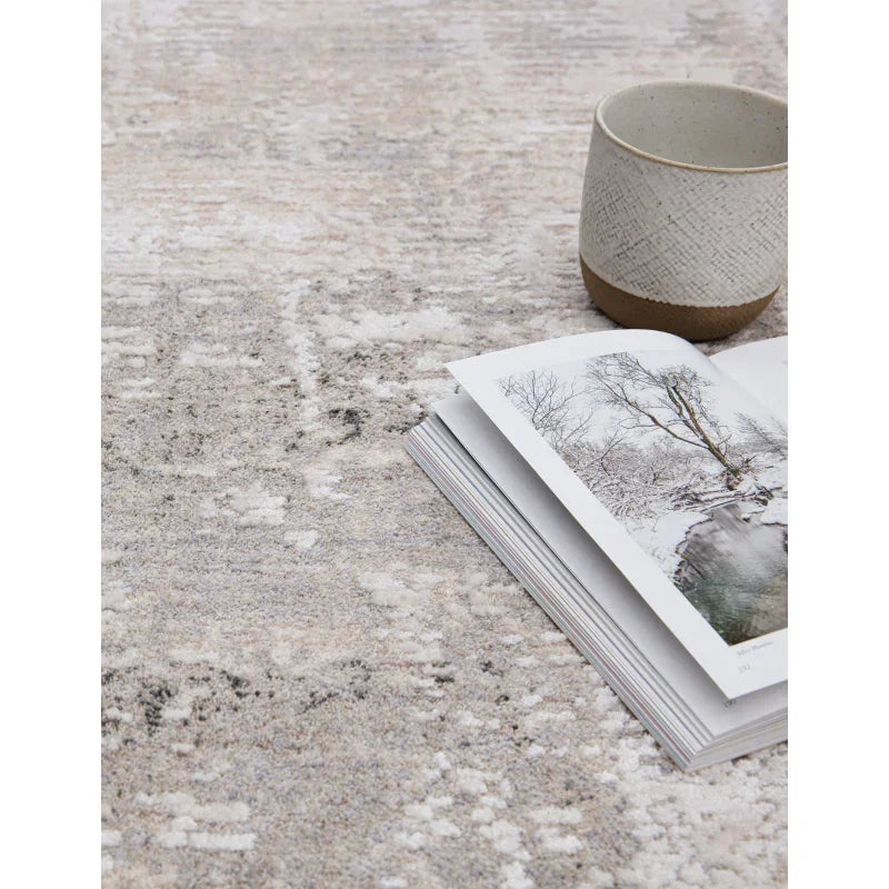 Soft grey patterned rug with ceramic mug and open book placed on top