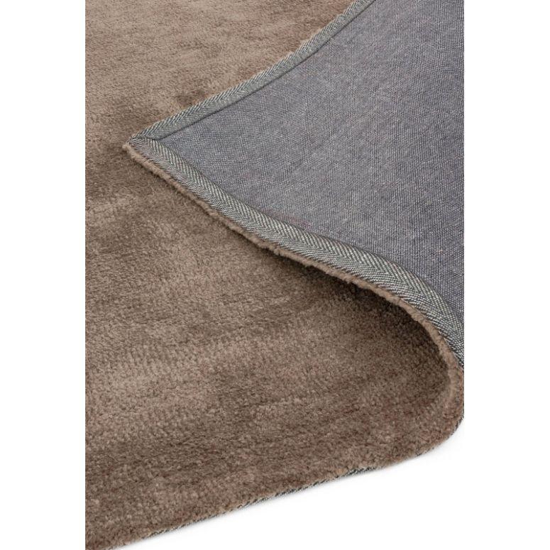 Close-up of brown area rug with grey backing corner folded