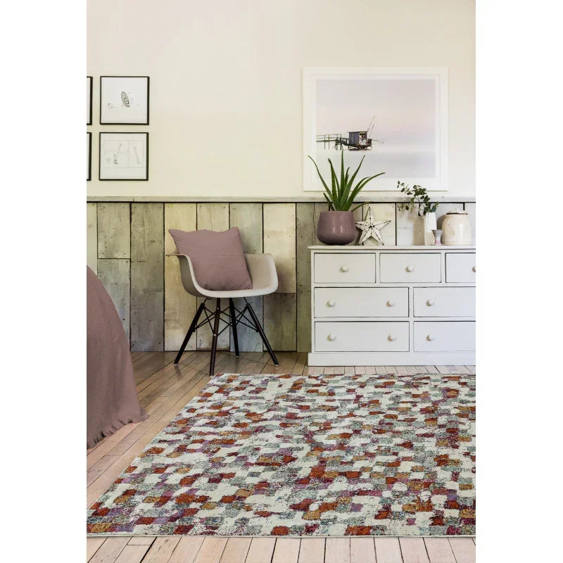 Multicoloured patterned area rug in modern bedroom with grey chair and white chest of drawers