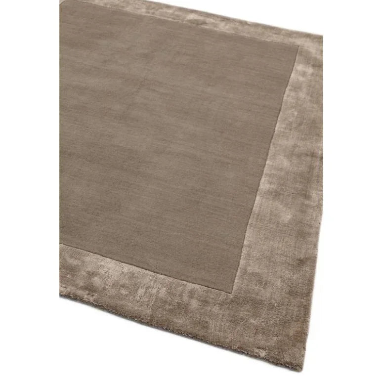 Taupe area rug with wide plush border and smooth central panel, shown from angled view