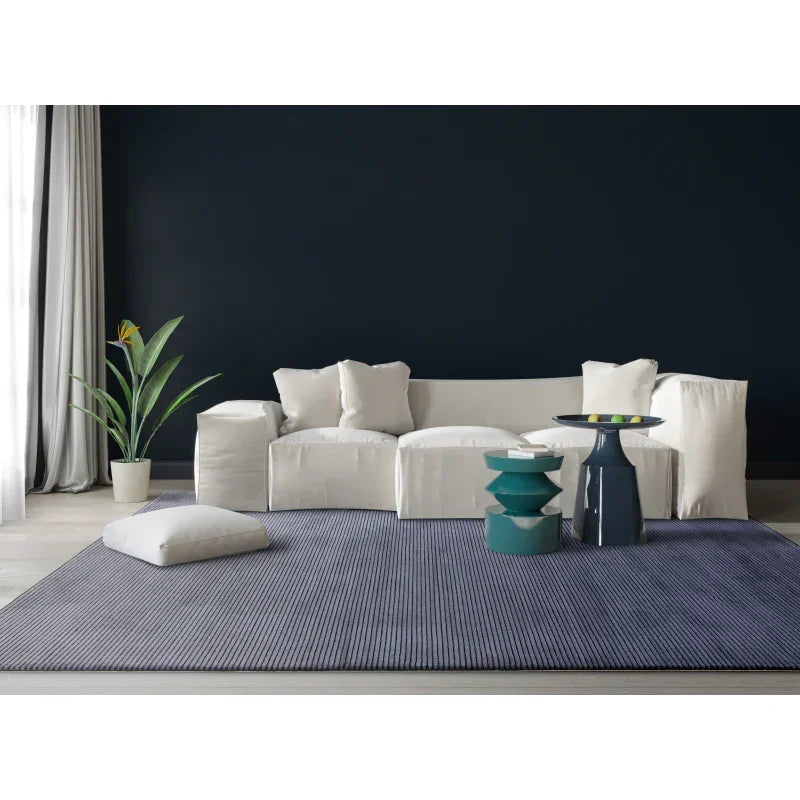 Modern living room with white sofa, grey area rug, green side tables, and potted plant