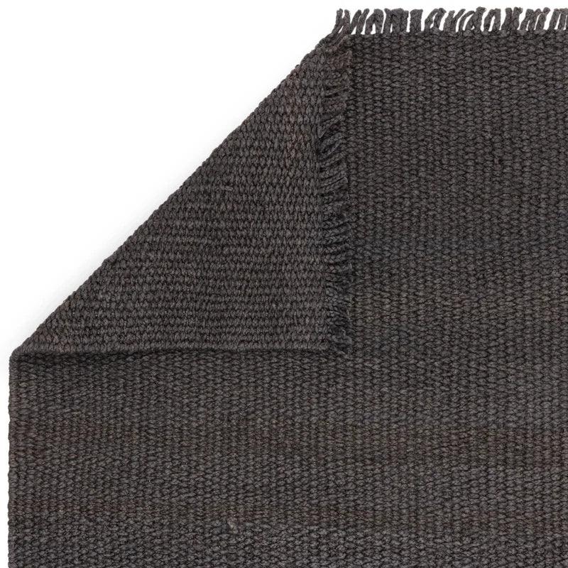 Dark grey woven rug with textured pattern and visible corner fold