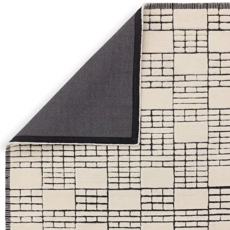 Modern geometric area rug with cream and black grid pattern, corner folded to show backing