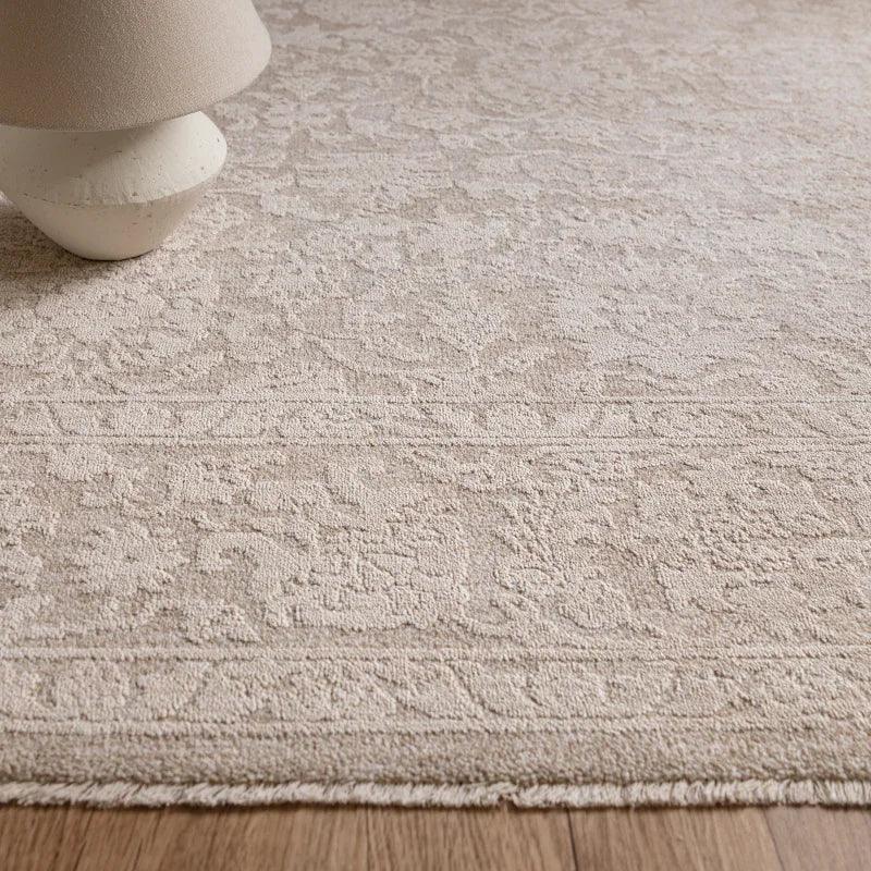 Beige textured rug with subtle pattern and fringed edge on wooden floor