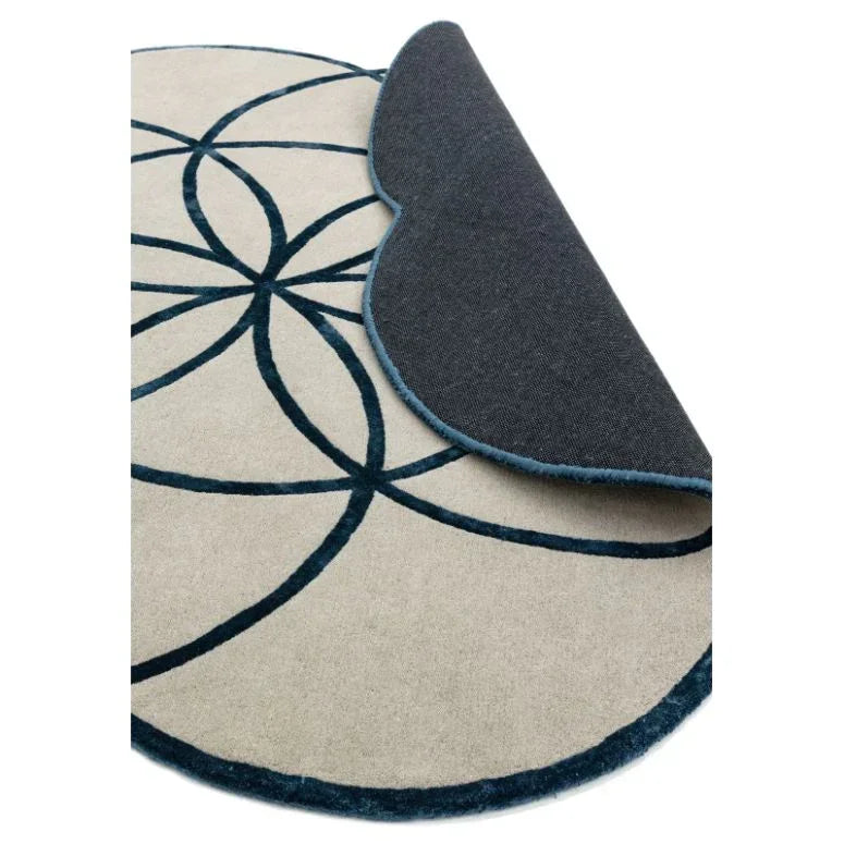 Round beige and blue rug with geometric pattern, edge flipped to show backing