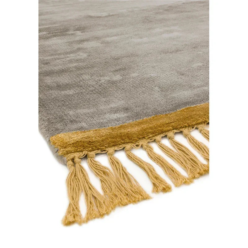Grey area rug with gold tasseled edge and soft textured surface