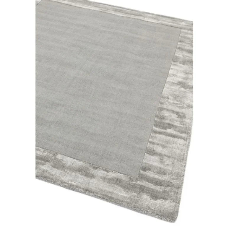 Grey area rug with wide textured border and smooth central panel, corner view