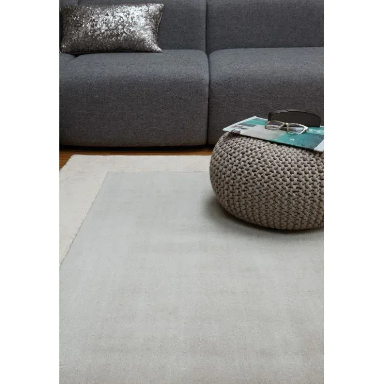 Light grey rug in living room with chunky knit pouf and modern grey sofa
