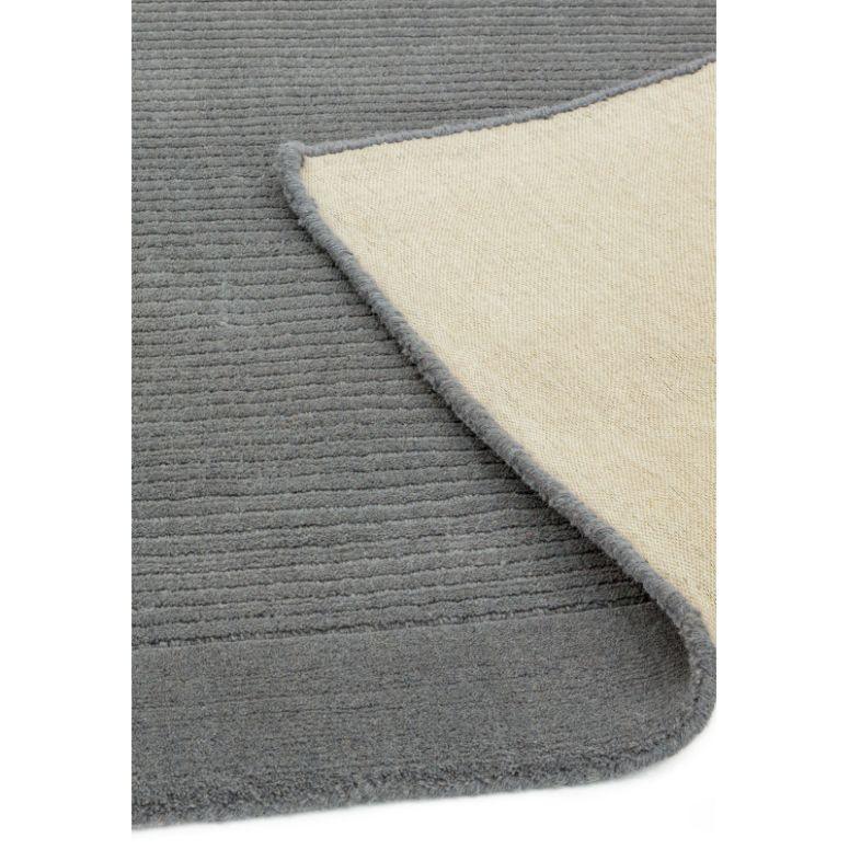 Grey textured area rug with one corner folded to show beige woven backing