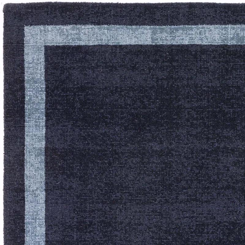 Navy blue area rug with light blue border and textured finish, close-up corner view
