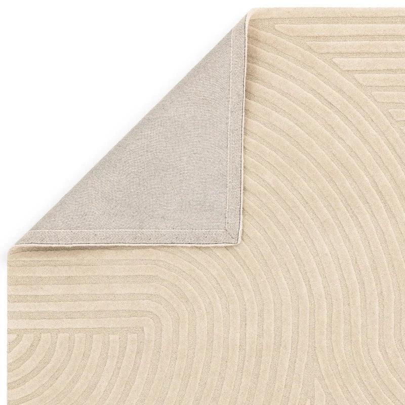Beige area rug with textured geometric pattern, close-up of corner fold and backing