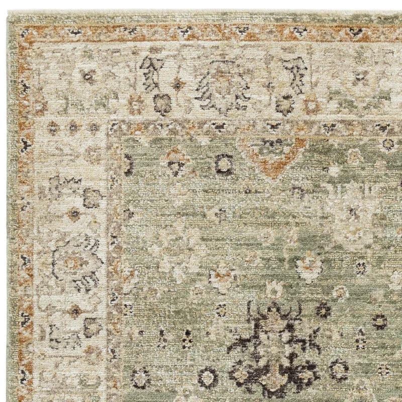 Corner detail of green patterned area rug with cream and beige floral motifs