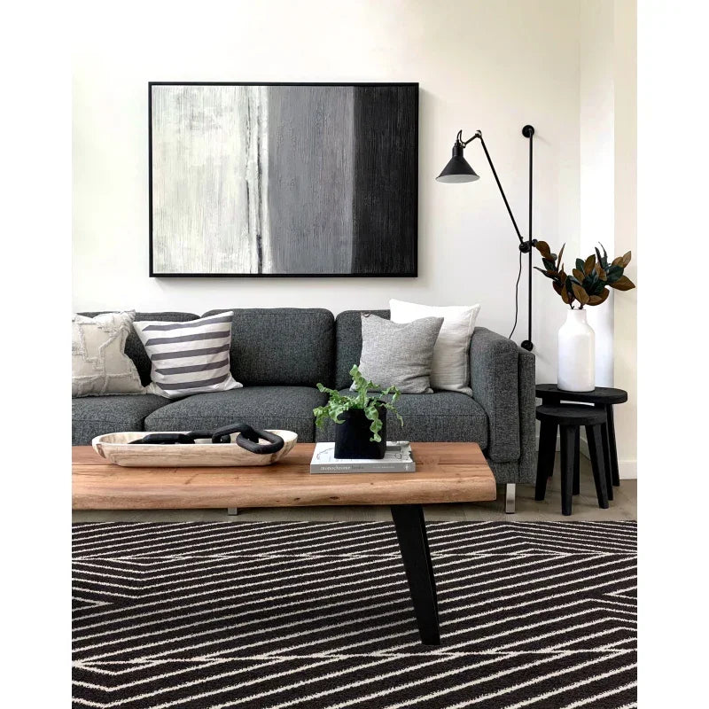 Grey fabric sofa with neutral cushions, wooden coffee table, and modern striped rug in living room