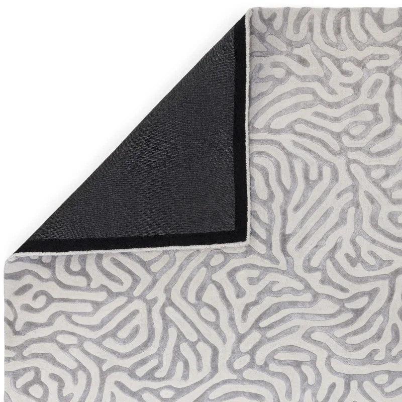 Grey patterned area rug with abstract lines, corner folded to show black underside