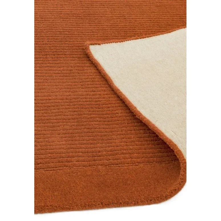 Burnt orange textured area rug with visible corner flipped to show backing