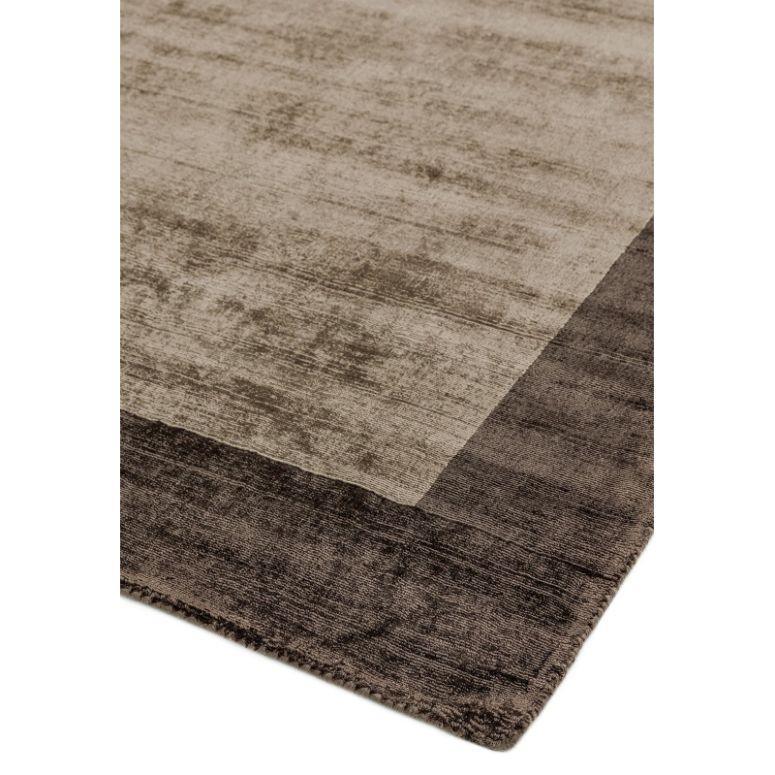 Beige and brown area rug with subtle stripe pattern and dark border, corner angled view