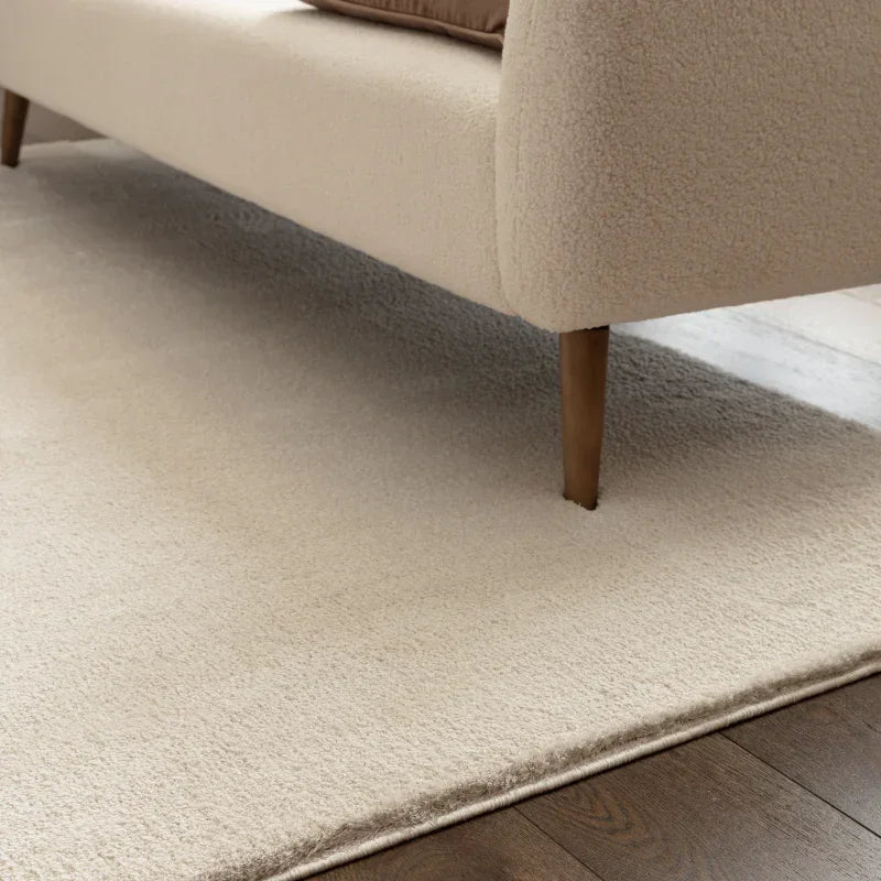 Beige wool rug under cream sofa with wooden legs on hardwood floor