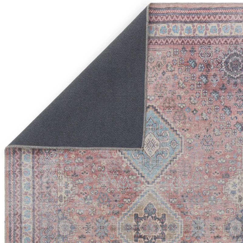 Vintage style area rug with pink and blue geometric pattern, corner flipped to show backing