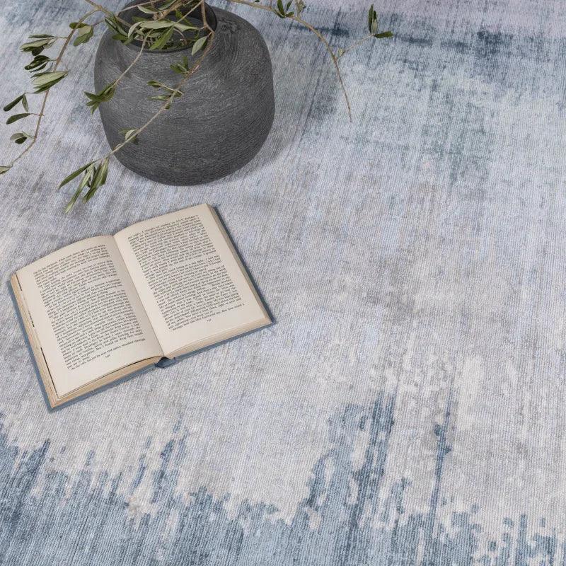 Light grey and blue area rug with open book and dark vase with green branches