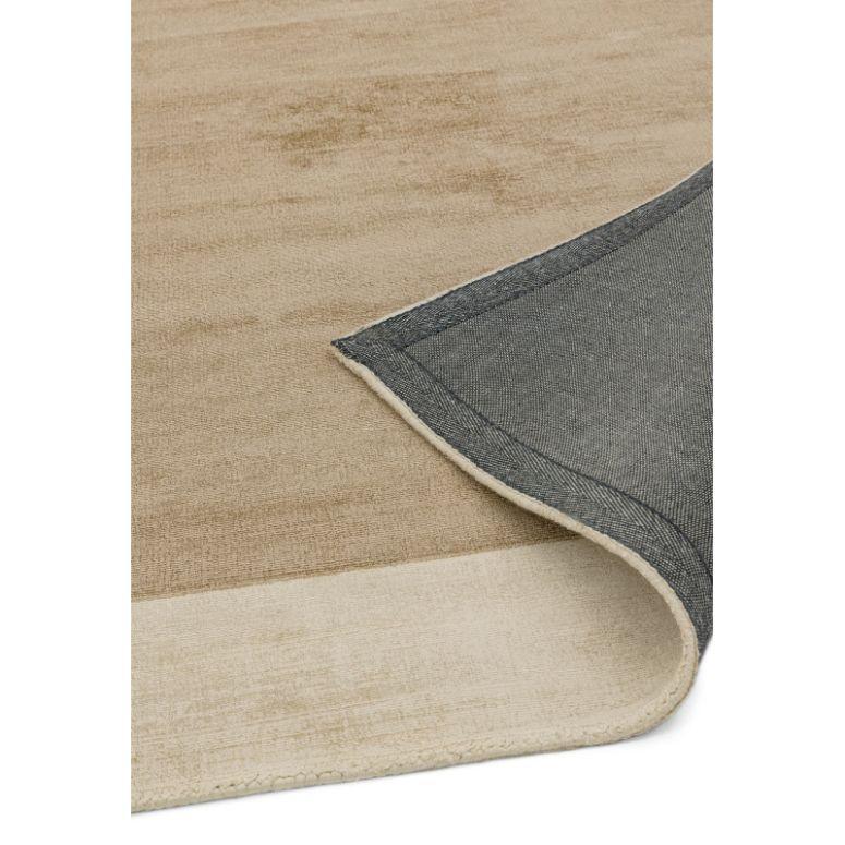 Beige area rug with visible corner folded to show backing and textured surface