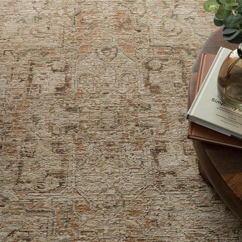 Beige patterned rug beside a round wooden table with books and a glass vase
