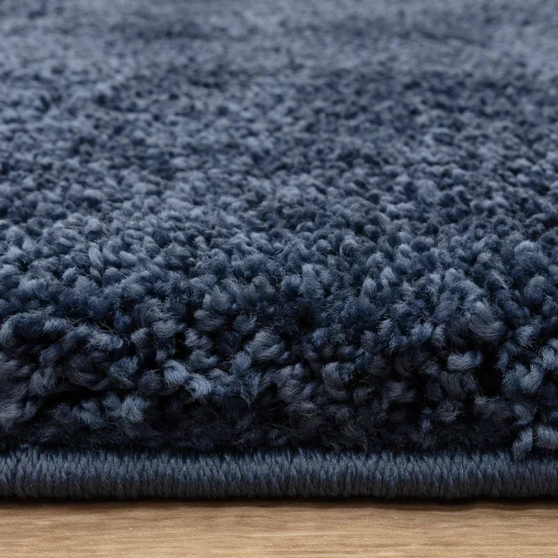 Close-up of dark blue shaggy rug pile and edge on wooden floor