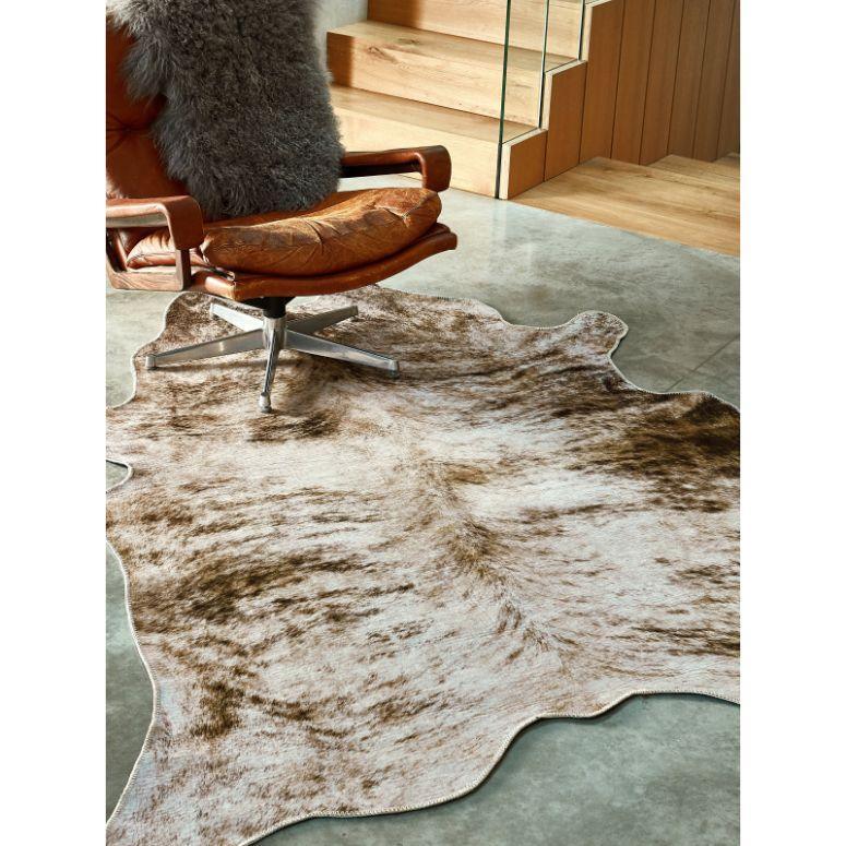 Brown and white cowhide rug on polished concrete floor beside leather chair