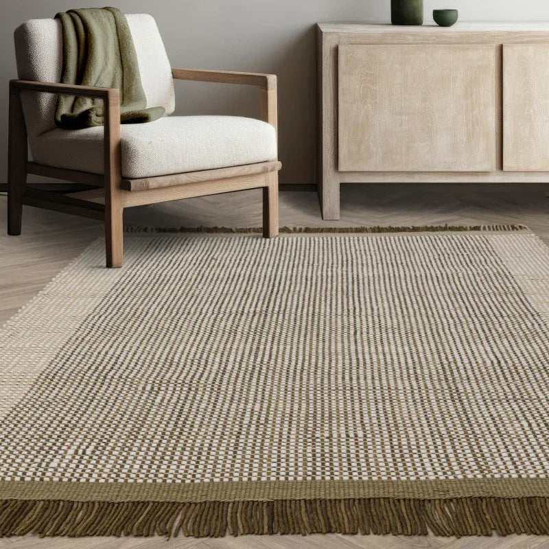Beige and olive woven rug with fringe in modern living room with neutral armchair