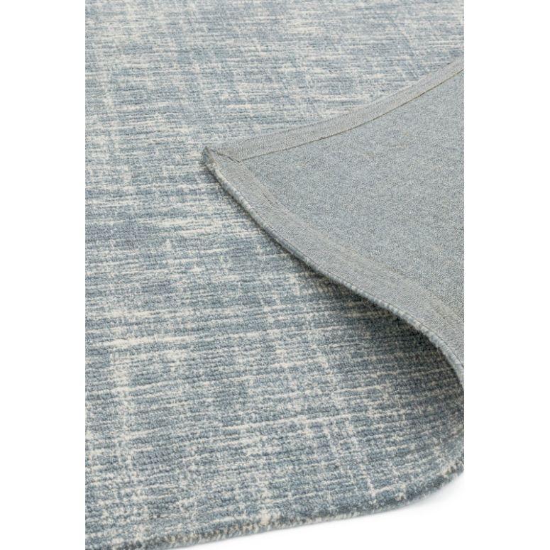 Blue textured area rug with subtle pattern and corner flipped to show backing