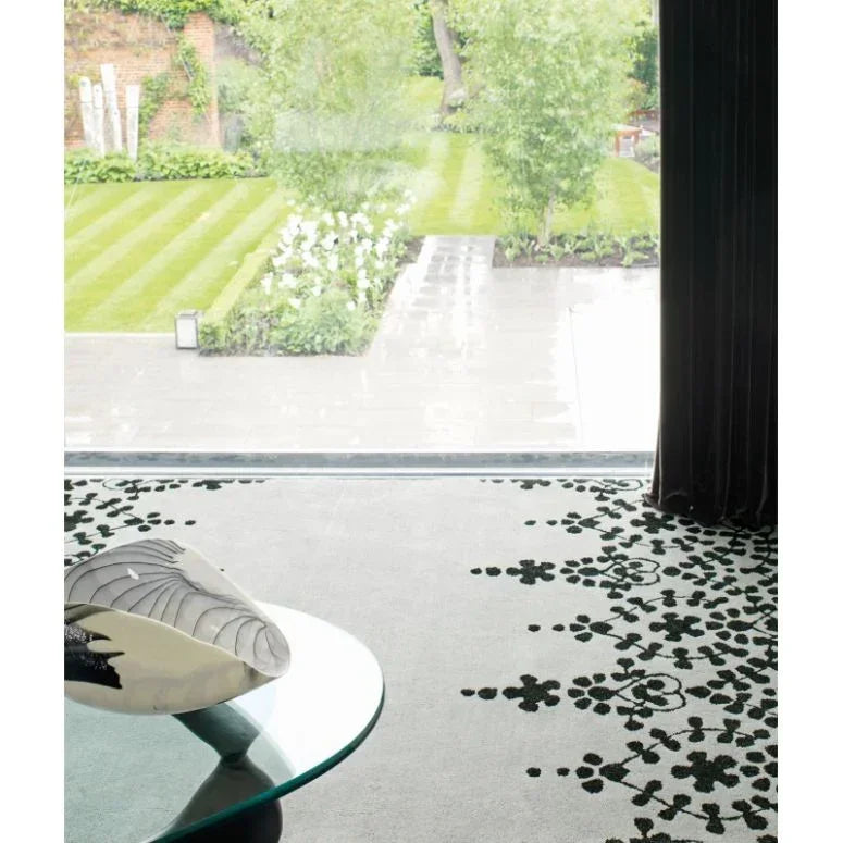 Modern rug with black floral pattern on light floor beside glass coffee table in living room