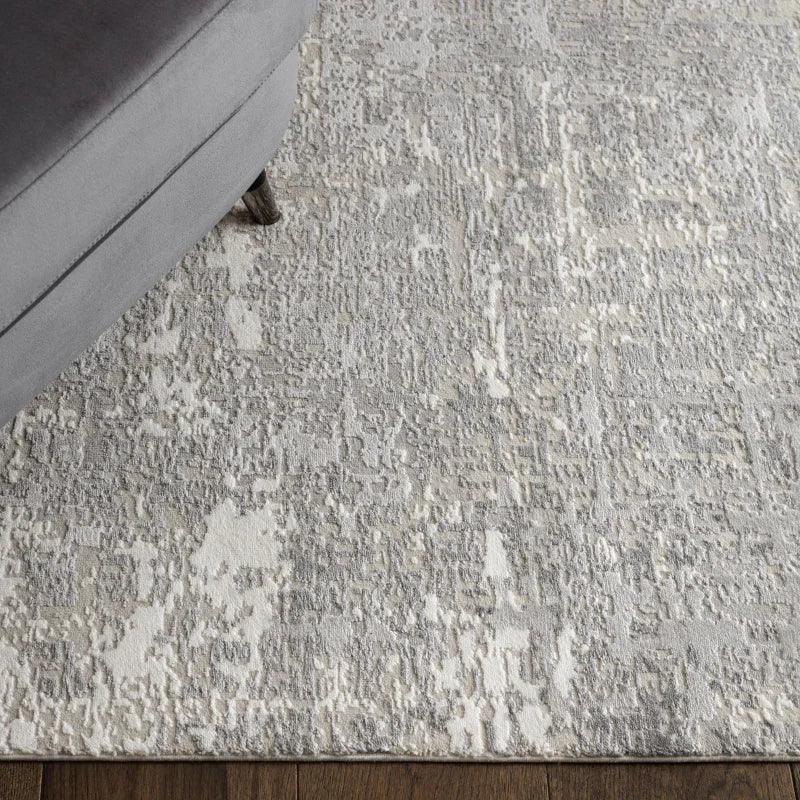 Textured grey area rug with abstract pattern beside grey upholstered sofa on wood floor
