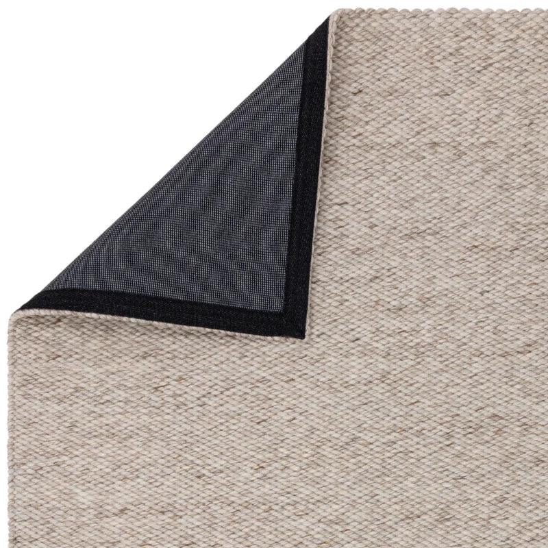 Beige woven rug with black non-slip corner backing detail