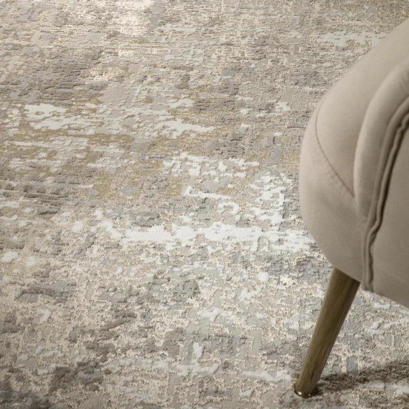 Abstract beige and grey area rug under beige upholstered chair leg