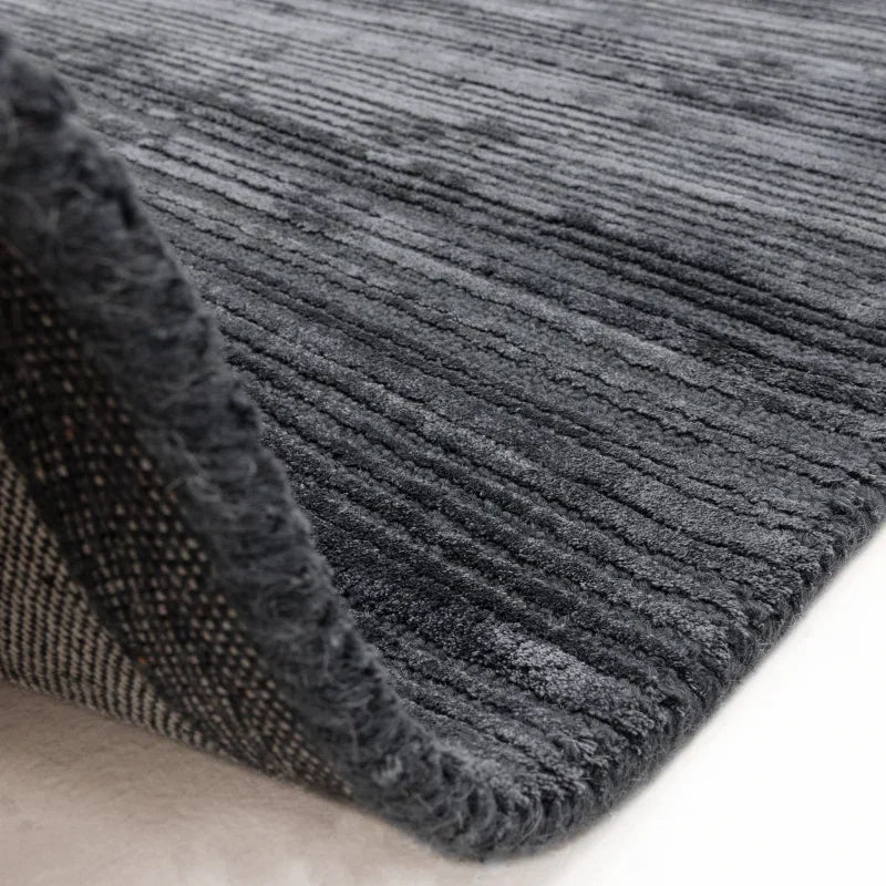 Textured grey rug with striped pattern and soft pile, close-up corner view