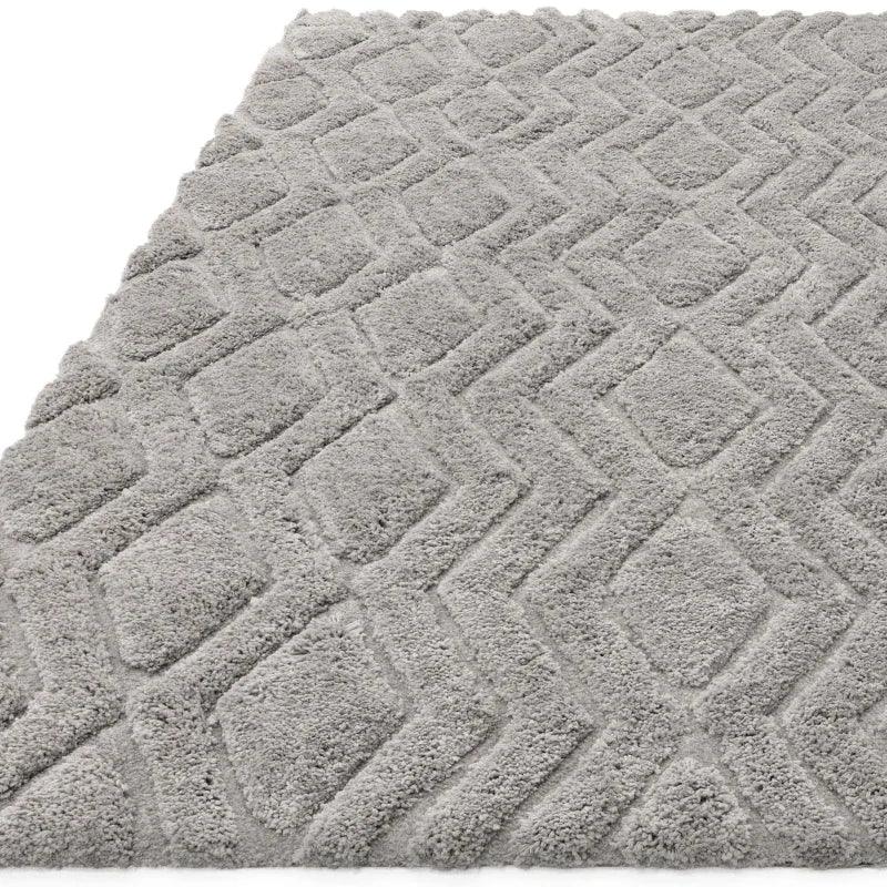 Light grey textured rug with geometric diamond pattern and soft pile, angled corner view