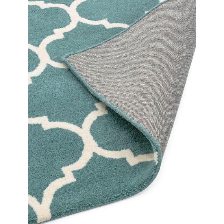 Blue patterned rug with white geometric design and grey backing, corner folded over
