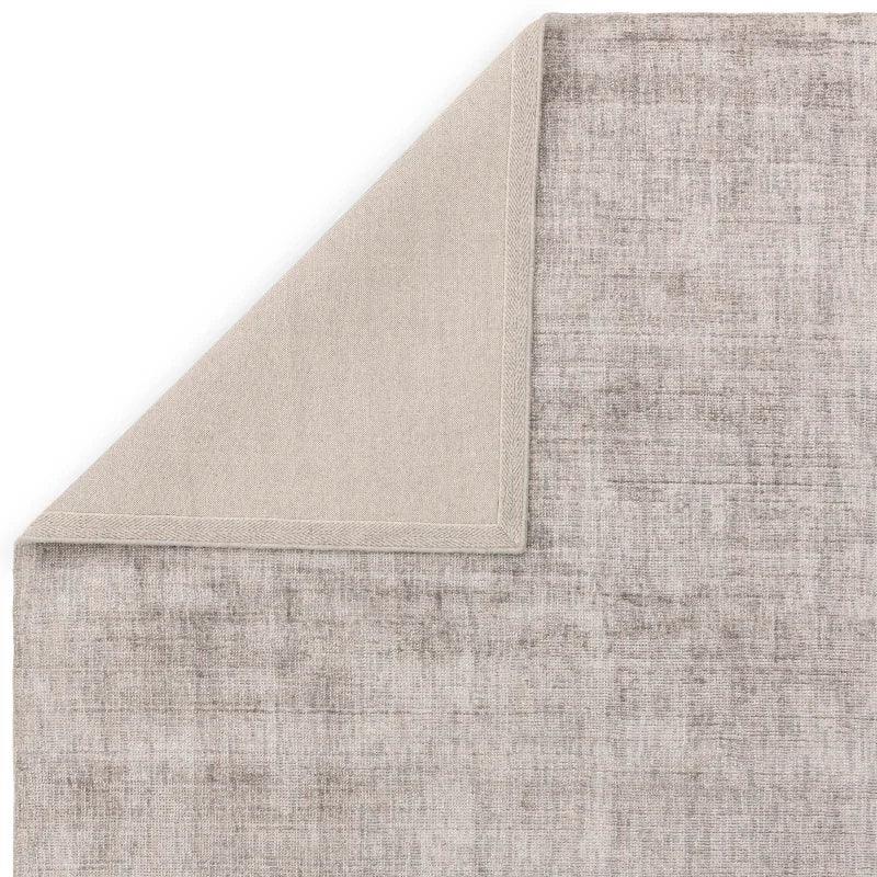 Grey textured area rug with visible corner folded over showing underside fabric