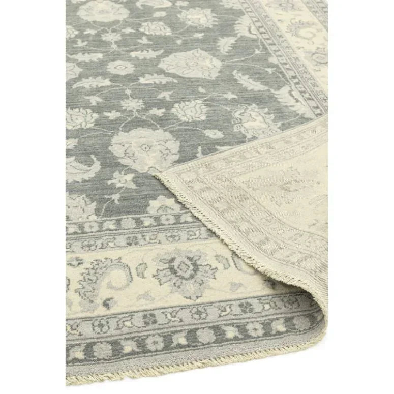 Grey floral patterned rug with cream border, one corner folded to show underside