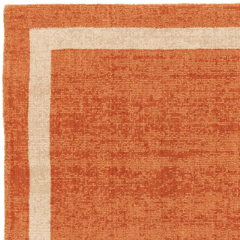 Burnt orange area rug with cream border and textured weave, corner close-up view