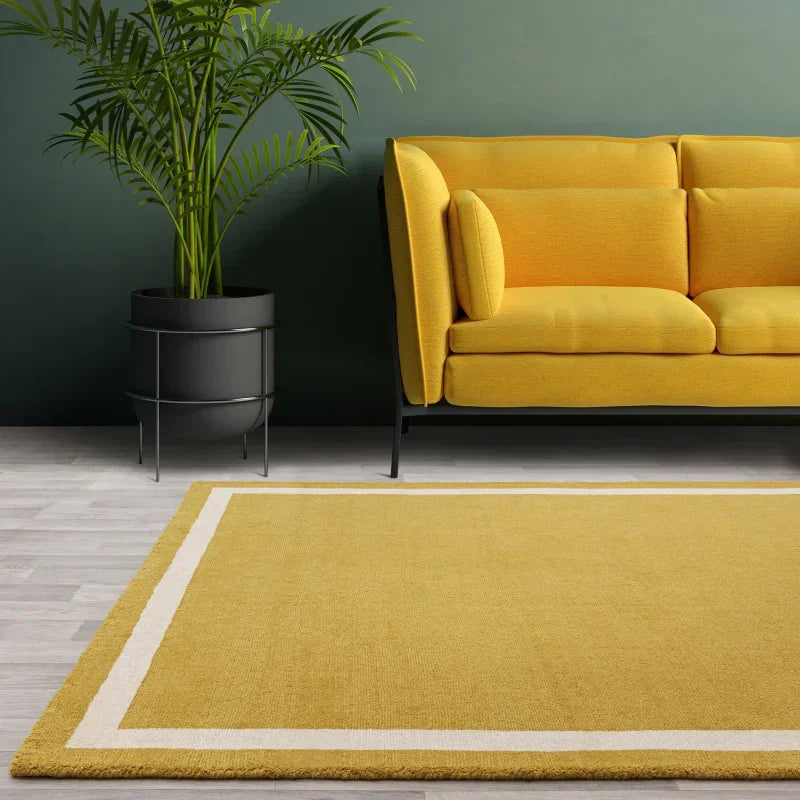 Yellow sofa with black legs next to green plant and yellow bordered rug on light wood floor
