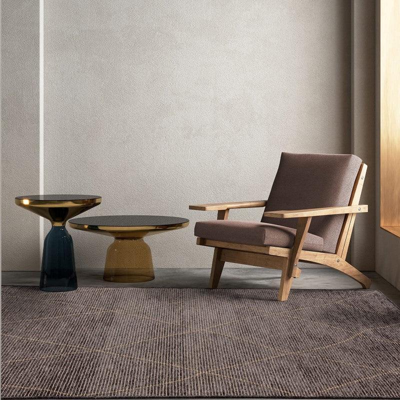 Modern lounge chair with wooden frame beside two glass side tables on textured rug