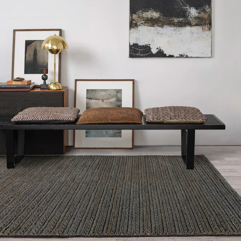 Modern bench with textured cushions on grey rug, decorative art and lamp in background